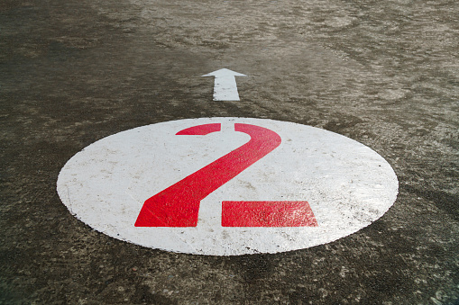 Red number two inside a white circle and an arrow painted on concrete background - 45 degrees angle view, closeup, landscape format