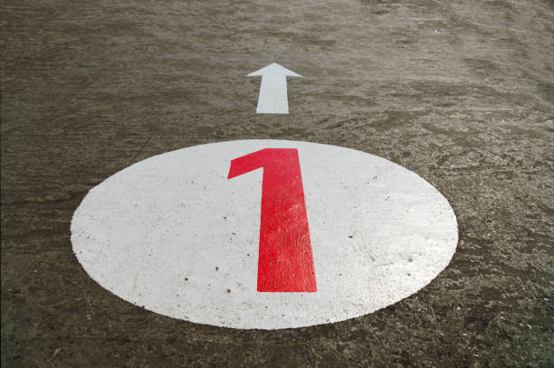 Red number one inside a white circle and an arrow painted on concrete background - 45 degrees angle view, closeup, landscape format