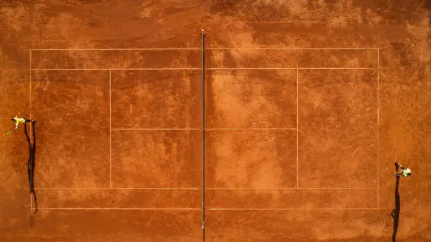 Tennis clay court seen from above with two men playing match. They are mature adult, and very agile and healthy. Photo made with drone.