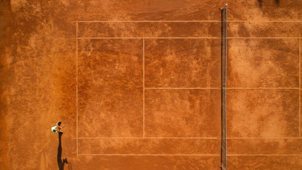 One tennis player on clay court One part of tennis clay court with one man player only. He is mature adult, and very agile and healthy. Photo made with drone, directly above. clay court stock pictures, royalty-free photos & images