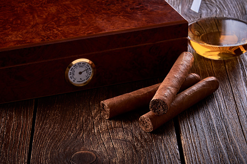 Bodegón con caja de madera para humidificación, tres puros y vaso de whisky sobre mesa vieja. photo