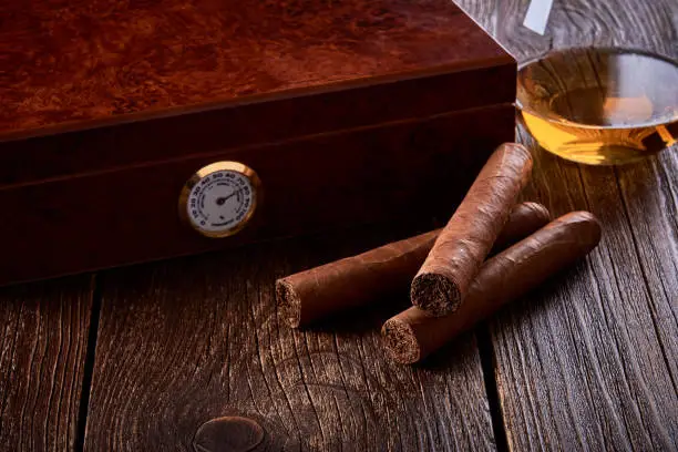 Still life with wooden box for humidification, three cigars and glass of whiskey on old table.