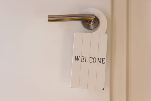 white welcome sign with writing hanging decoratively at restroom door inside a house. Doorknob made of stainless steel.