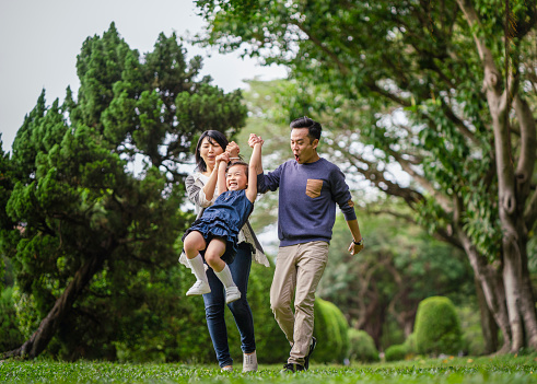Cheerful parents lifting daughter while walking on field. Happy family enjoying leisure time at park. They wearing casuals.