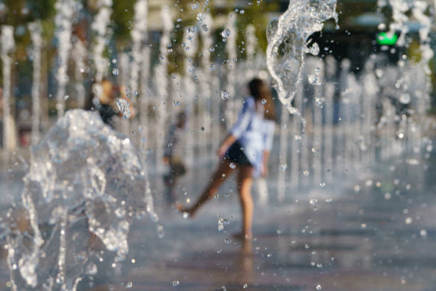 Photography of barefoot girls touching the fountain by legs.  Image with defocued background. Concepts of walking, happiness, childhood and freshness in hot summer day.