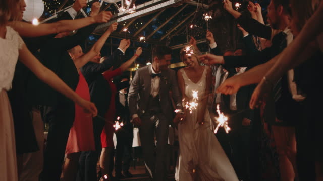 Guests holding sparklers over running newlyweds