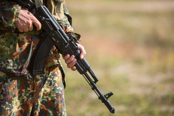 A man in camouflage holds a rifle in hands, close-up. Soldier on the battlefield with a black machine gun ak 47 bullets stock pictures, royalty-free photos & images