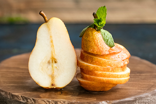 Fresh pears on a wooden board, cut into pieces, decorate with mint leaves. Copy space for your text. dark background