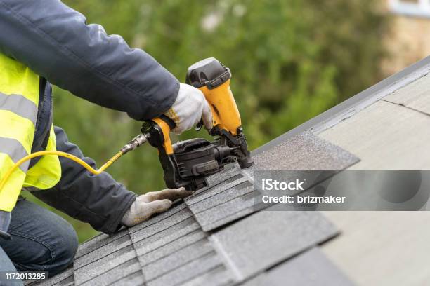 Workman Using Pneumatic Nail Gun Install Tile On Roof Of New House Under Construction Stock Photo - Download Image Now