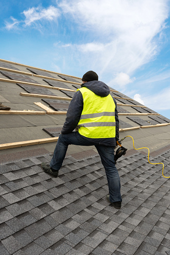 Trabajador usando pistola neumática de clavos instalar teja en el techo de la nueva casa en construcción photo