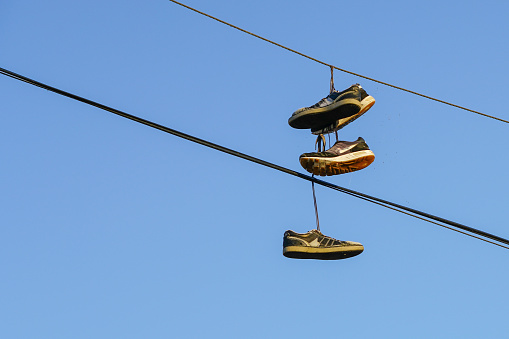 Several tennis shoes on power lines in front of a clear blue sky.
