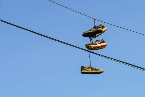 Photo of Several tennis shoes on power lines in front of a clear blue sky.