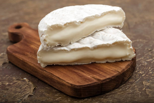 Soft cheese with white mold on a cutting board, with vegetables