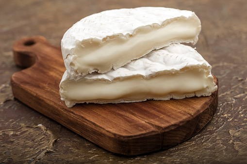 Soft cheese with white mold on a cutting board, with vegetables. Snack to wine