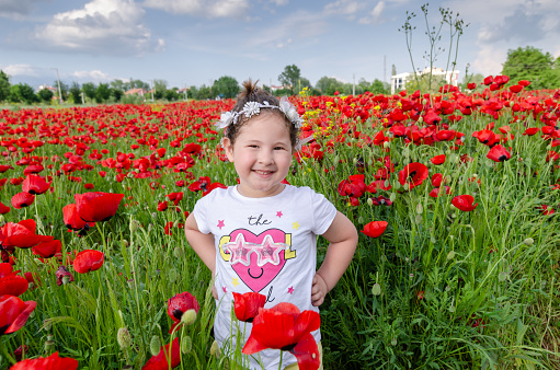 Beautiful kid in poppy field in the summer months.She is smile.