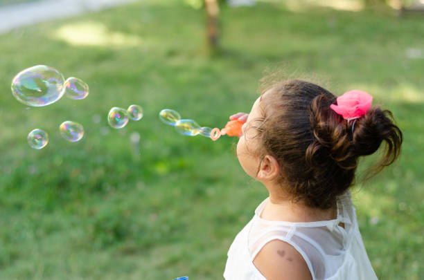 Cute girl is blowing soap bubbles in the garden.
