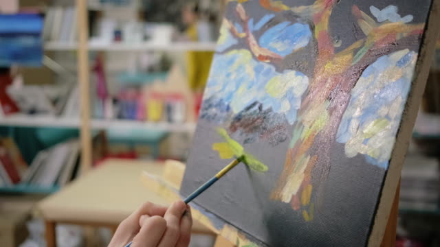 Artist is applying yellow gouache on black canvas in art school, close up