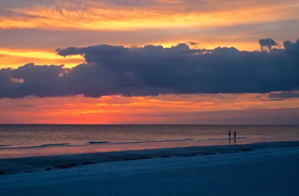 Beautiful cloudy sunset at Siesta Key, Florida, with people in silhouette in the foreground.