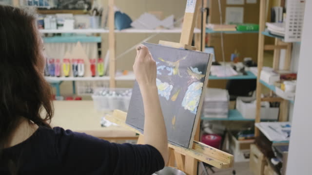 Woman artist is making strokes by paints in workshop, drawing a picture