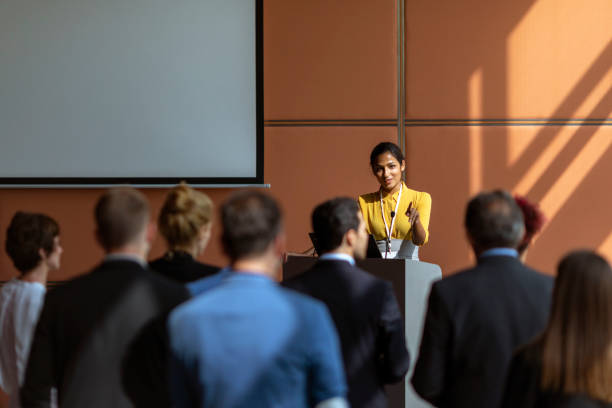 Businesswoman speaking to the audience An Indian female presenter interacting with the audience at a business presentation in the board room press conference photos stock pictures, royalty-free photos & images