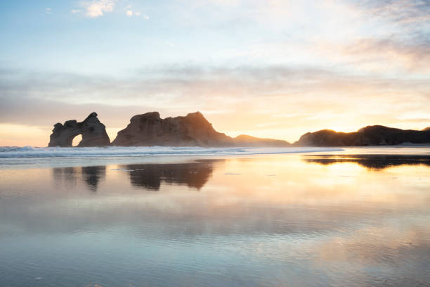 New Zealand winter sunrise Winter sunrise at Wharariki Beach at the top of New Zealand's South Island. The clouds are colored by the rising sun. The rocks are the Archway Islands. This beach is a popular tourist destination and is know for it's beautiful reflections of the islands. nelson landscape beach sand stock pictures, royalty-free photos & images