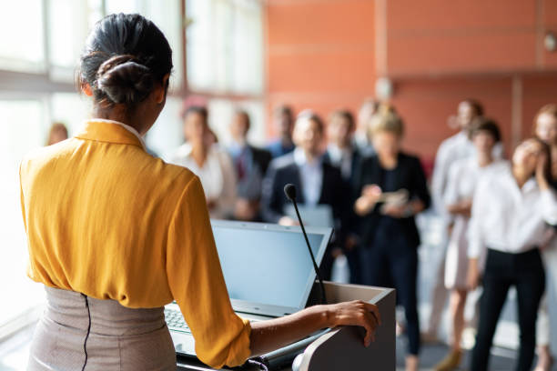 Public speaker An Indian female presenter at a conference, audience in the background summit meeting photos stock pictures, royalty-free photos & images