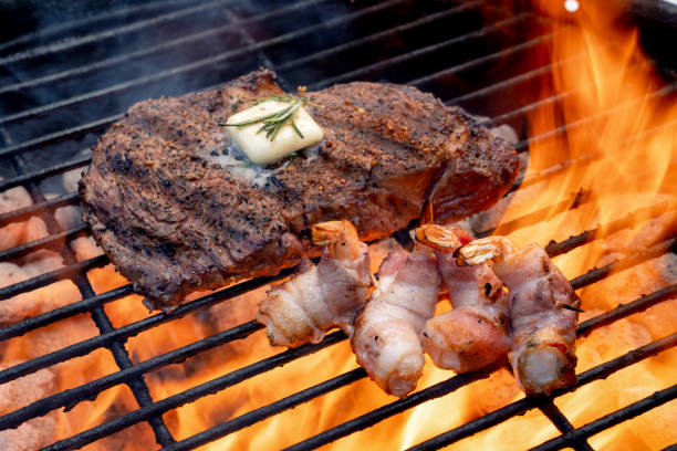 crevettes enveloppées de bacon sur un gril ardent avec un steak de boeuf délicieux d'oeil de côte - surf and turf prepared shrimp seafood steak photos et images de collection