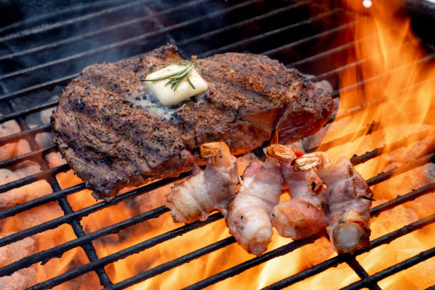 bacon-wrapped shrimp on a fiery grill with a delicious rib eye beef steak - surf and turf prepared shrimp seafood steak imagens e fotografias de stock