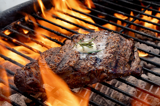 Grilled Rib Eye Steak of an authentic Charcoal Barbecue with Flames Kissing the Meat t oLock in the Flavor