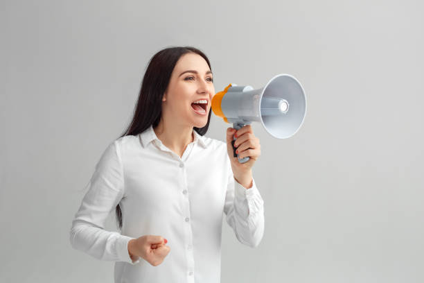 Freestyle. Woman standing isolated on gray speaking at megaphone cheerful stock photo