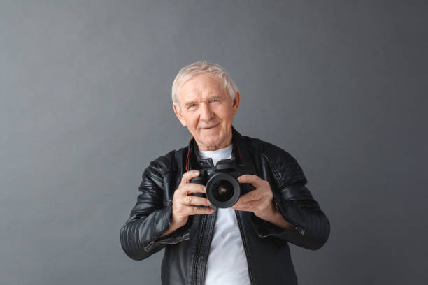 istock Senior man in leather jacket standing isolated on gray holding camera happy 1172072800