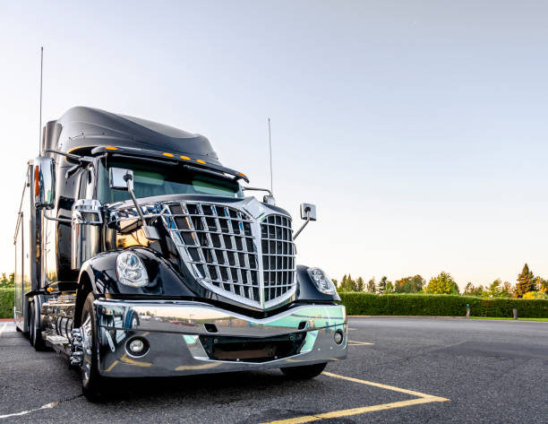 Black stylish big rig semi truck with bright chrome grille stand on wide parking lot Big rig classic American idol black industrial semi truck with chrome grille and commercial cargo in dry van semi trailer standing on the truck stop parking lot at twilight time reflection sunlight radiator grille stock pictures, royalty-free photos & images