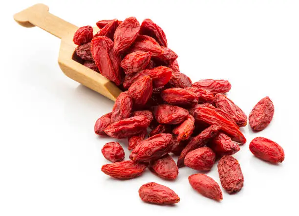 Dried Goji berries in a wooden serving scoop. 
Isolated on a white background.