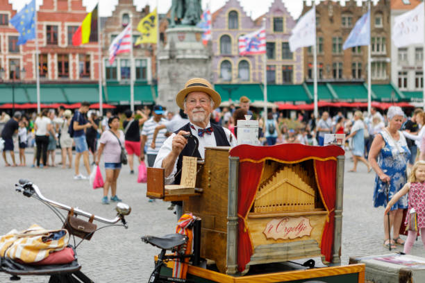 Belgian street folk music performer in national suits. Man plays music on barrel organ in Grote Markt Square in Bruges, Belgium. The Markt of Bruges is located in the heart of the city.