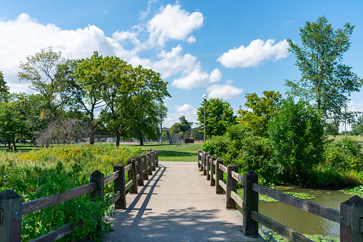 A bridge over a stream with green trees and plants in Humboldt Park in Chicago during the summer
