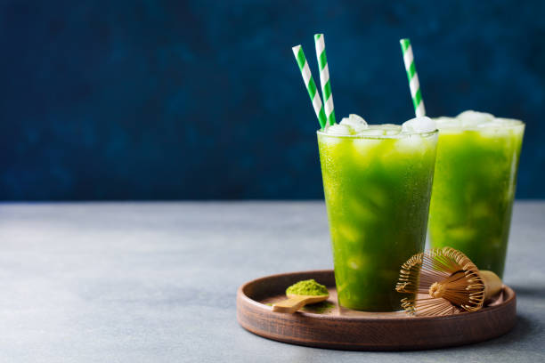 Matcha ice tea in tall glass on wooden plate. Blue background. Copy space. Matcha ice tea in tall glass on wooden plate. Blue background. Copy space green tea cocktail bar stock pictures, royalty-free photos & images