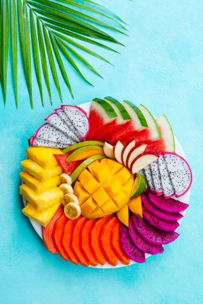 istock Tropical fruits assortment on a white plate with palm leaf. Blue background. Top view. 1172116482
