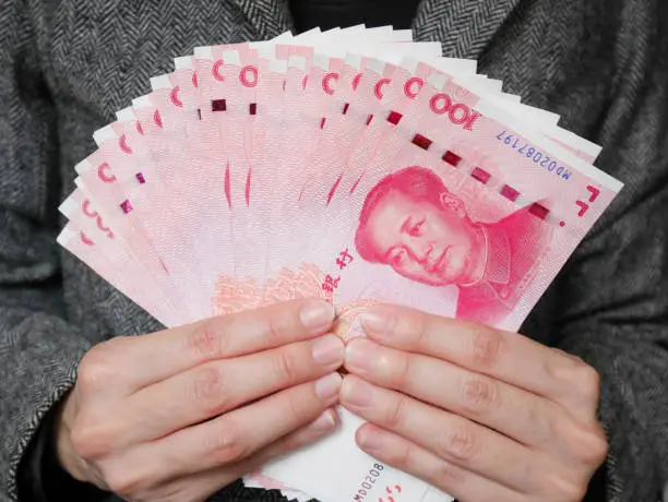 Business woman holding stack of 100 yuan banknotes money. Chinese yuan currency