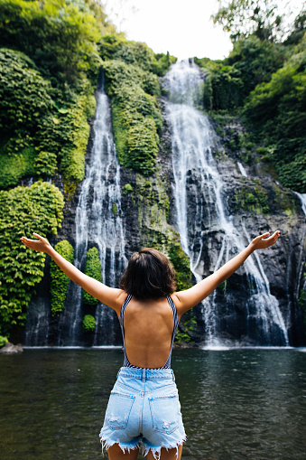 Happy woman with raised arms enjoying life at Banyumala twin waterfall