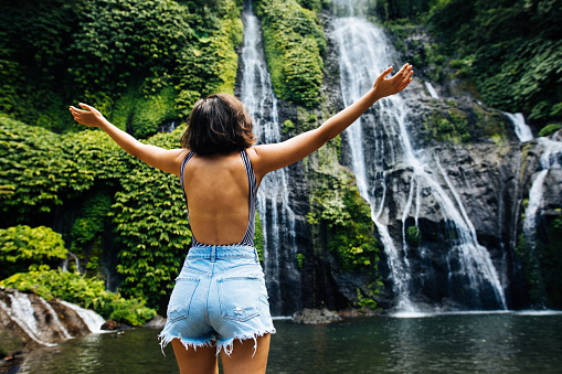Happy woman with raised arms enjoying life at Banyumala twin waterfall