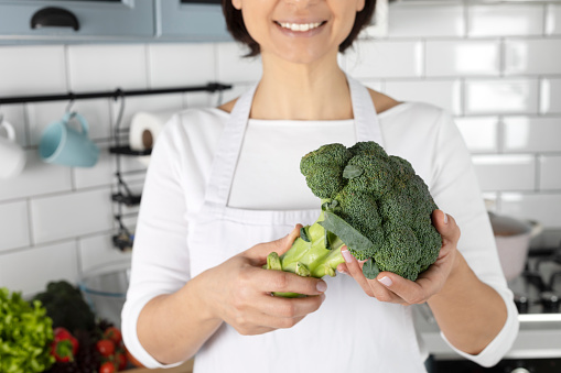 Unrecognizable female is holding broccoli in hand.