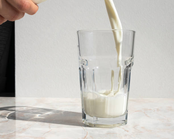 istock Milk from bottle pouring into glass staying on light table 1172129471