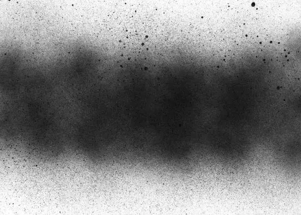 Photo of Subtle grit texture of black spray track on white paper. Particles and blots of paint