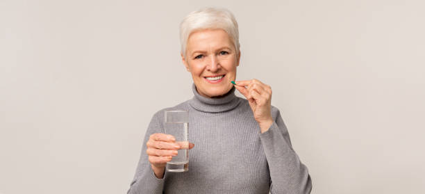 istock Beautiful elderly woman taking vitamin supplements over light studio background 1172135752