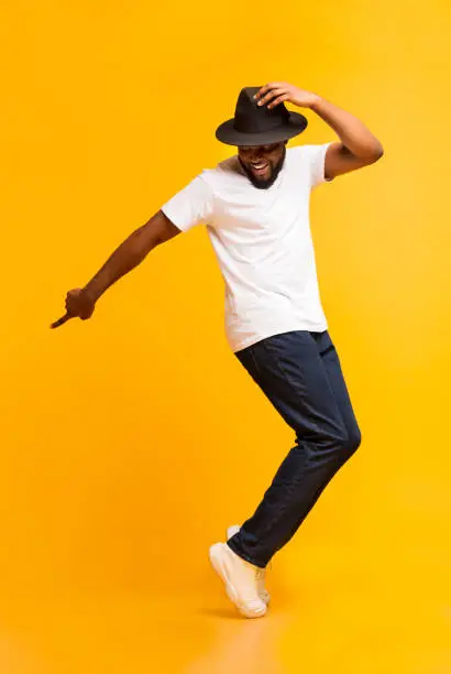 Photo of Young cheerful man dancing on tiptoes on yellow studio background