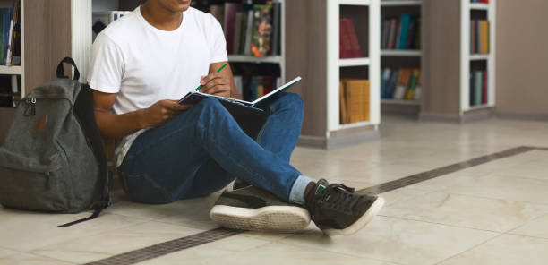 istock Creative male student writing essay, sitting on floor at library 1172136629