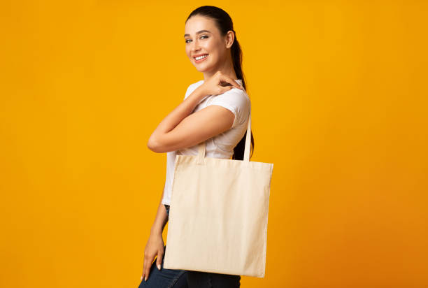 年輕女子拿著白色生態袋在黃色工作室背景 - 環保袋 個照片及圖片檔