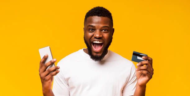 Emotional millennial guy with smartphone and credit card I made it. Emotional millennial guy with smartphone and credit card, panorama with copy space stubble male african ethnicity facial hair stock pictures, royalty-free photos & images