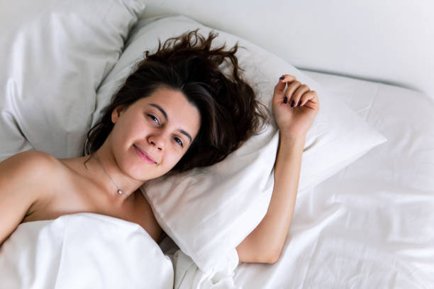 istock pretty brunette woman in bed with white sheets overhead view 1172138405