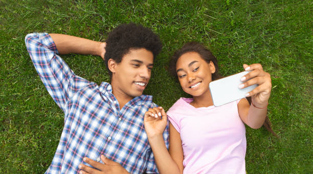 Teenage couple making selfie while laying on grass African american teenage couple making selfie while laying on grass, panorama teen romance stock pictures, royalty-free photos & images